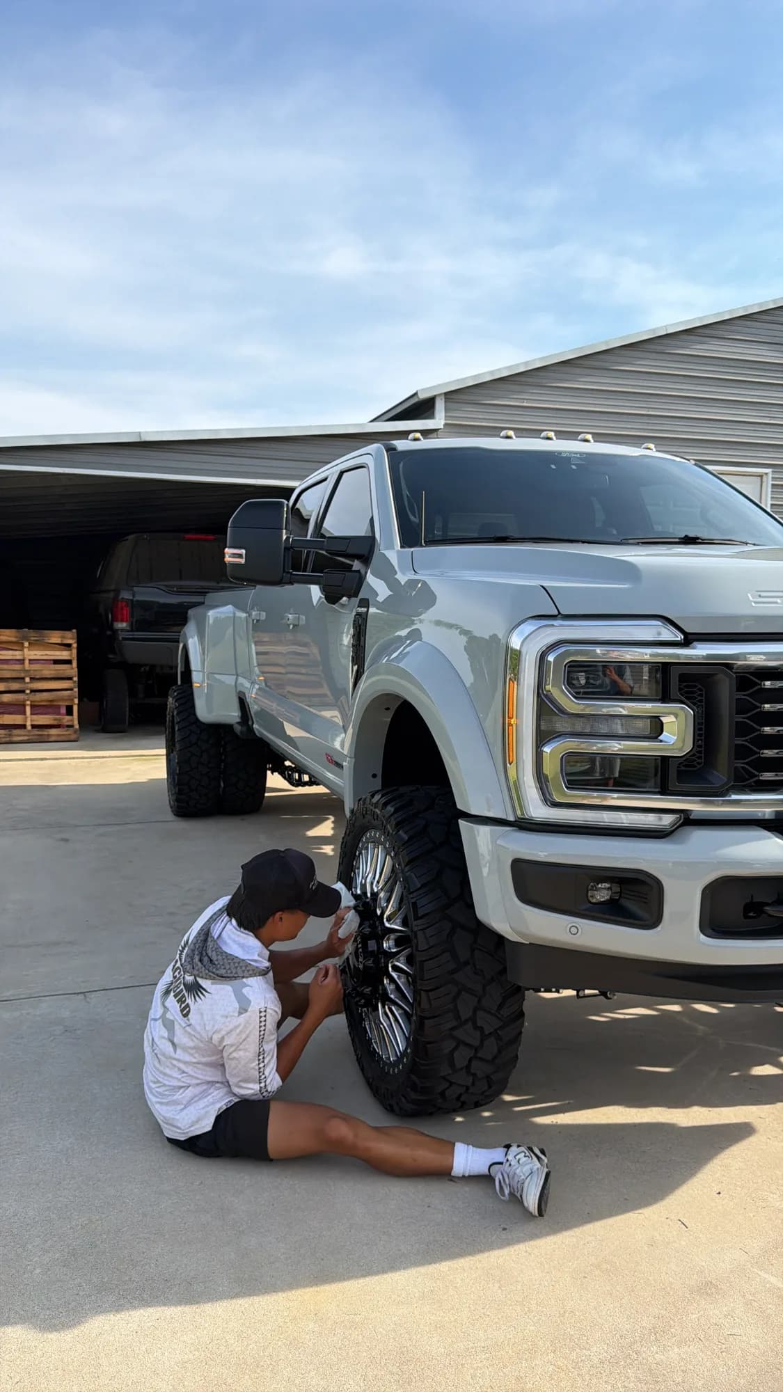 A Blackbird technician seated on the driveway cleaning the wheel of a lifted Ford Super Duty dually